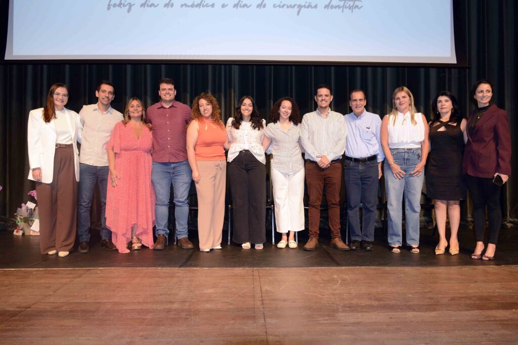 Grupo de responsáveis técnicos das unidades de saúde alinhados no palco para a fotografia oficial durante a solenidade.