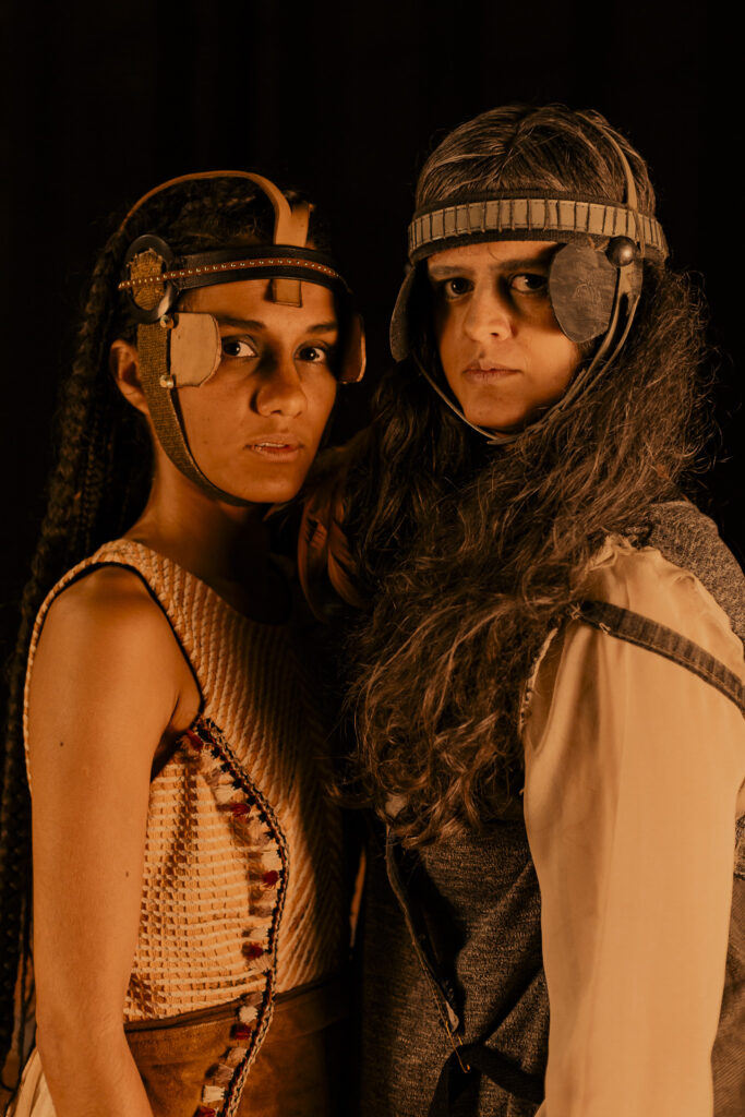 Retrato de estúdio focado nos rostos de duas atrizes que protagonizam o espetáculo "Mary para Mary". Elas usam adereços de cabeça curiosos e olham sérias para a câmera