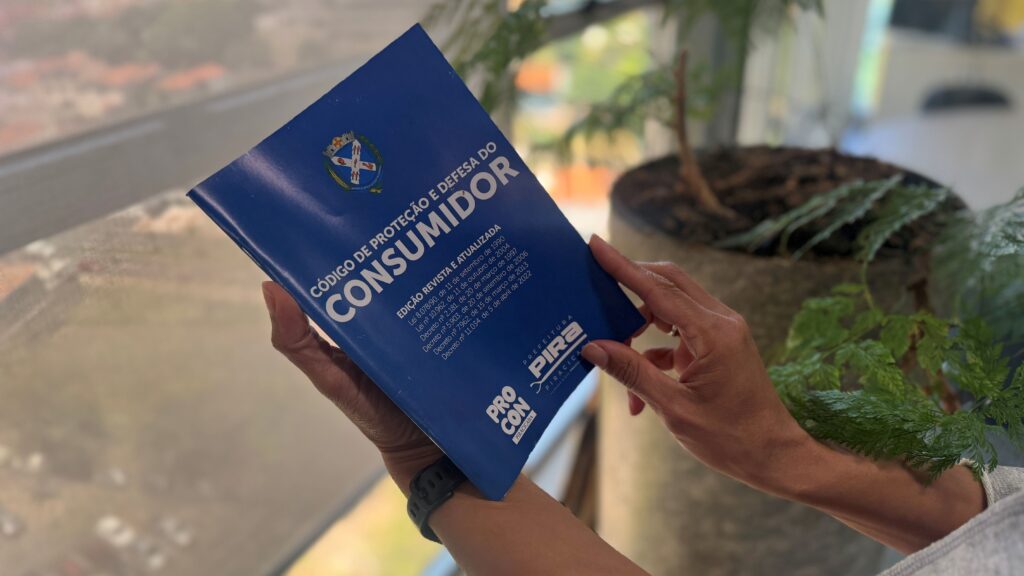 A imagem exibe as mãos de uma pessoa a segurar um exemplar impresso em tom azul do Código de Proteção e Defesa do Consumidor