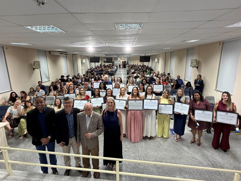 Visão ampla do auditório repleto de convidados e familiares, com todos os educadores premiados na frente a segurarem orgulhosamente os seus certificados.