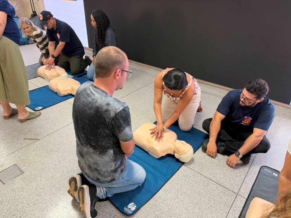 Participantes de um treinamento ajoelhados no chão a praticar manobras de reanimação cardiorrespiratória (RCP) em manequins de treino, sob a supervisão de instrutores do Samu.