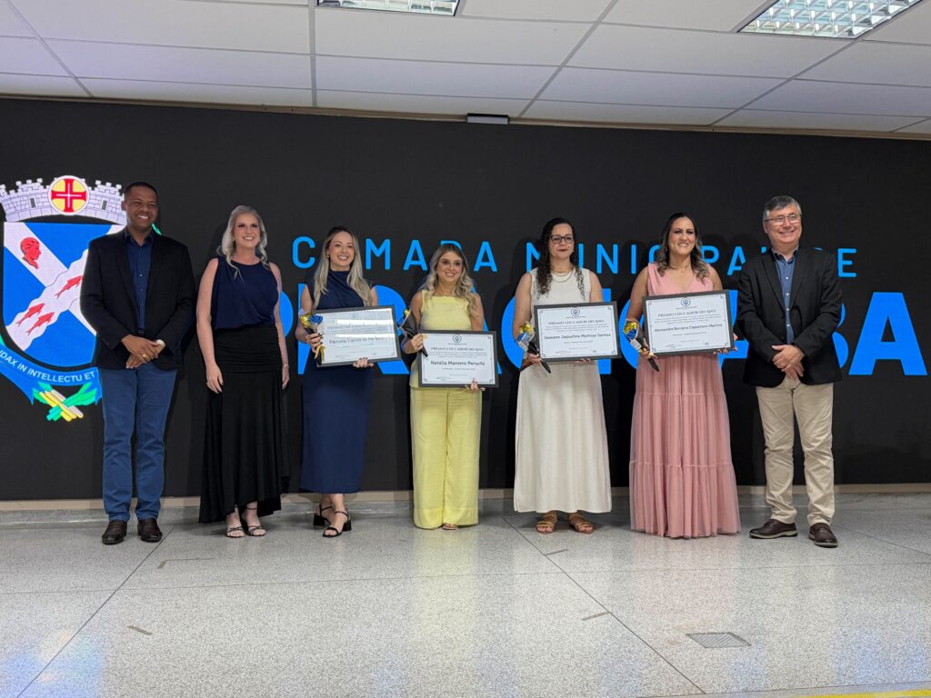 Grupo de professoras da categoria de Educação Infantil no palco, a exibir os seus quadros de certificado do prémio ao lado das autoridades locais.