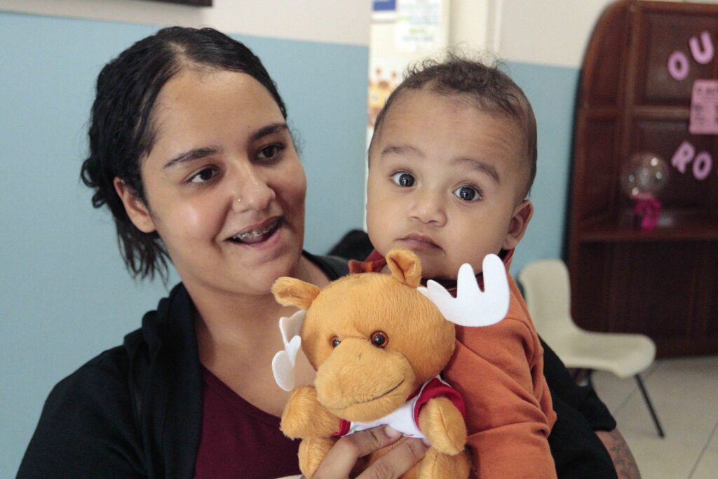 Raiane Solla sorri enquanto segura o seu filho bebé, Isaac, ao colo, acompanhado por um peluche de cervo.