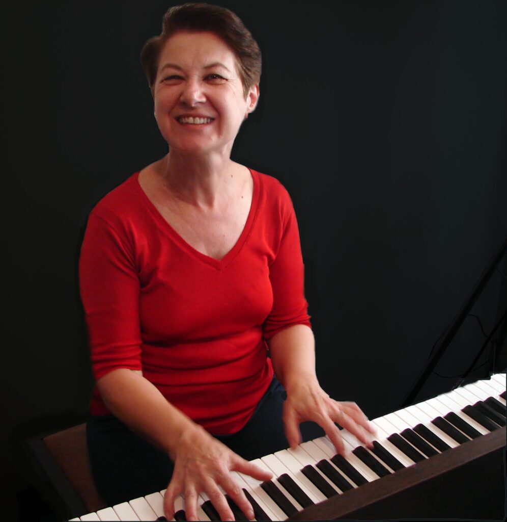 A pianista Regina Gomes sorri para a câmara enquanto toca teclado durante o espetáculo "Tocar... Cantar... Contar e Encantar".