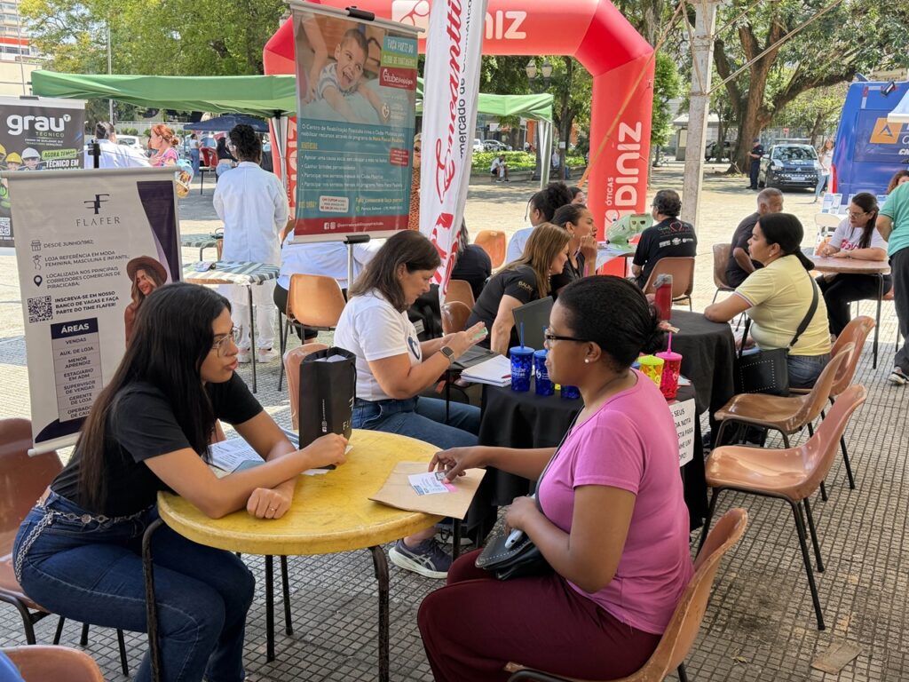 Tendas de atendimento ao ar livre com várias pessoas sentadas a mesas a conversar e a preencher documentos com os atendentes da acção.