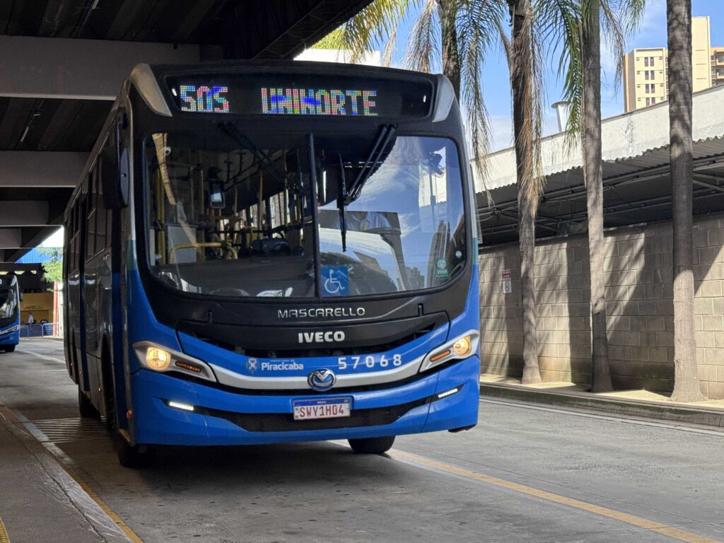Autocarro do transporte público de Piracicaba, nas cores azul e preto com a indicação da linha "505 UNINORTE" no painel luminoso, parado na plataforma de um terminal urbano ao lado de palmeiras.