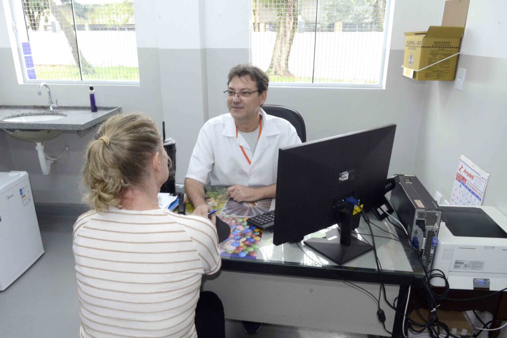 Um profissional de saúde de bata branca atende uma paciente numa consulta individual num gabinete médico de uma unidade de saúde.