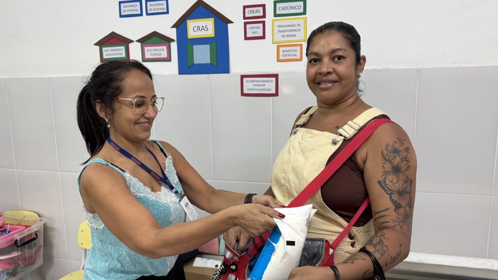 A assistente social Vilmarina Soares entrega pacotes de leite do programa social à beneficiária Maria Francisca, que os guarda numa bolsa térmica dentro da unidade do CRAS.